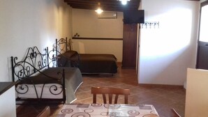 Ein kleines Zimmer mit einem Bett, einem Sessel, einem Tisch und einem Fernseher.