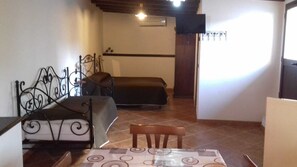 Ein kleines Zimmer mit einem Bett, einem Sessel, einem Tisch und einem Fernseher.