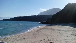 A beach with clear water, a sandy shore, and a mountain in the background.