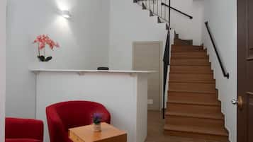A staircase with a wooden finish and a black handrail, leading to a landing with a white wall and a door.