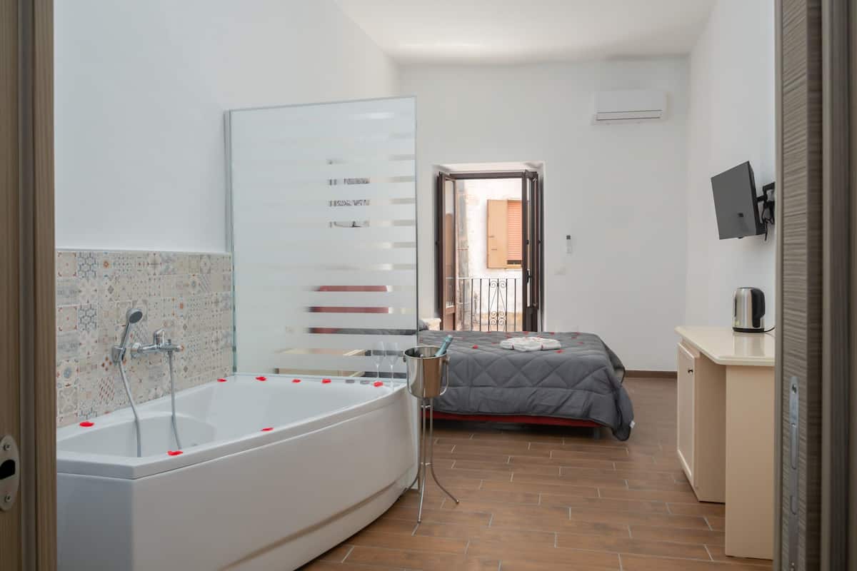Une salle de bain moderne avec une baignoire, une douche et un lit recouvert d’une couette grise.