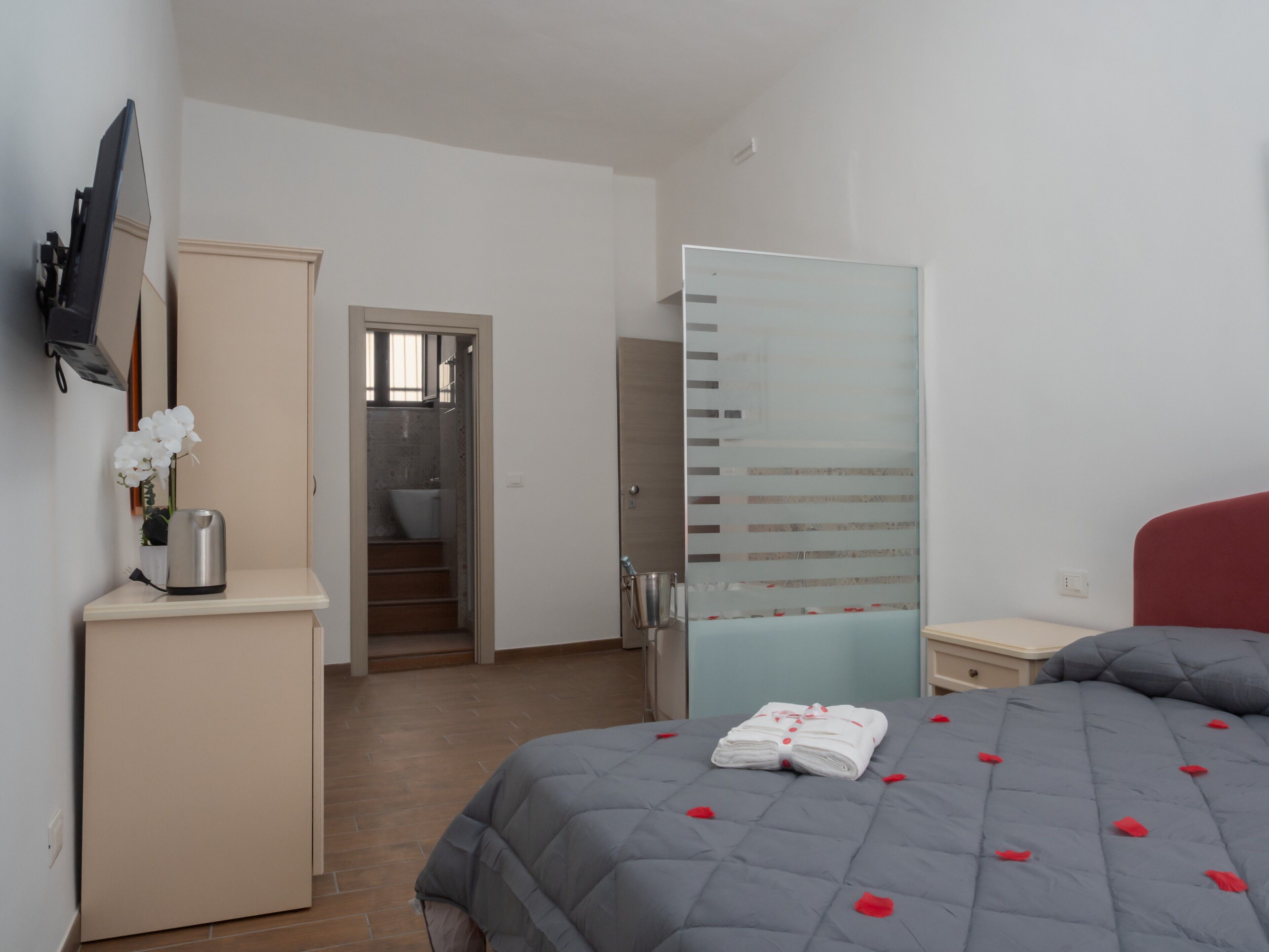 A bedroom with a bed, a wardrobe, a mirror, and a bathroom visible through an open door.