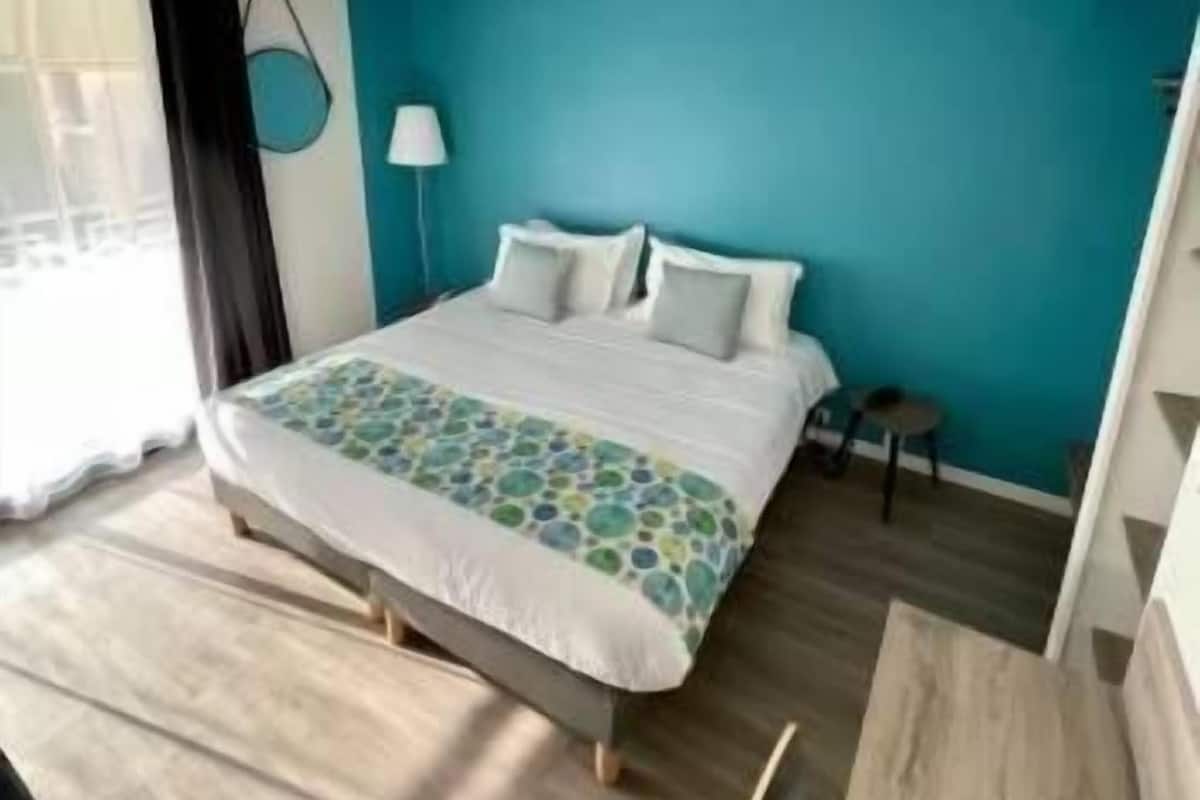 A bedroom with a bed, a desk, a chair, a lamp, and a window with curtains.
