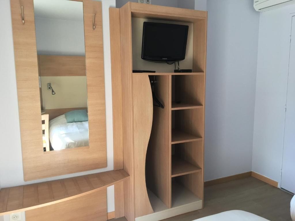 A bedroom with a wooden wardrobe, a mirror, a television on top, and a bed with a blue pillow.