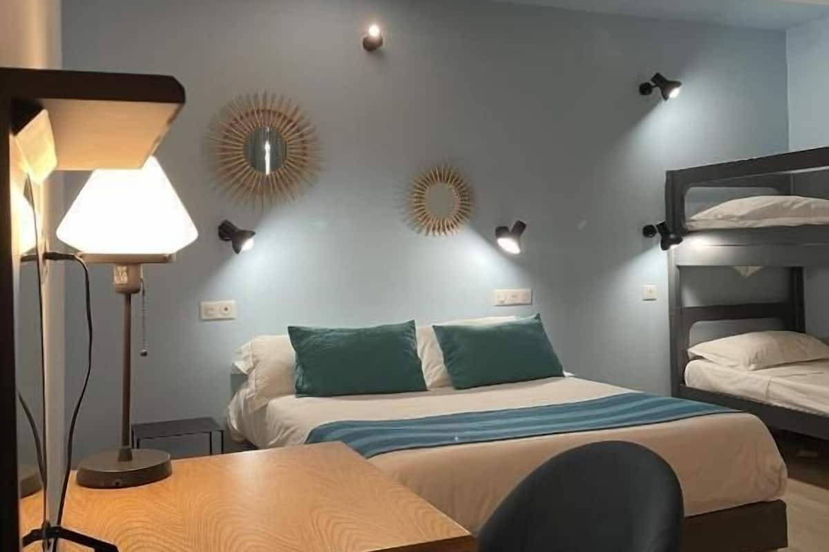 A hotel room with a bed, a desk, a chair, a lamp, and wall sconces.