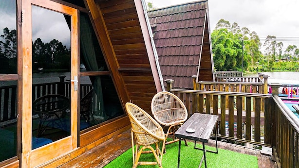 Eine Holzhütte mit geneigtem Dach, einem Balkon mit Tisch und Stühlen und Blick auf die umliegende Grünfläche.