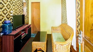 Ein Wohnzimmer mit Fernseher, Wasserspender, einem Rattan-Sofa und einer Holztür.