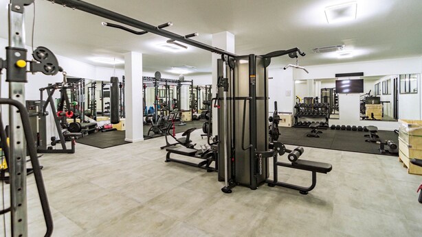Ein Fitnessstudio mit unterschiedlichen Trainingsgeräten, Spiegeln und einer sauberen, aufgeräumten Gestaltung.