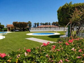 Une pelouse bien entretenue avec une piscine circulaire, entourée d’une clôture et de palmiers.
