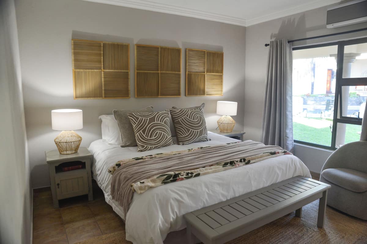 Una habitación de hotel con cama, lámparas de noche, un banco, una ventana con cortinas e iluminación en la pared.