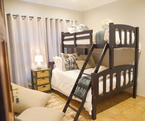 Una cama litera con escalera, una mesita de noche con lámpara y un pequeño aparador.