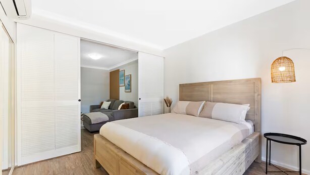 Un dormitorio con una cama grande, una mesita de noche, una lámpara de pared y una puerta corredera que da a otra habitación.