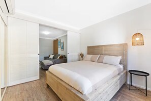 Un dormitorio con una cama grande, una mesita de noche, una lámpara de pared y una puerta corredera que da a otra habitación.