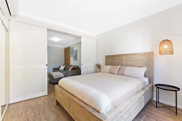 A bedroom with a large bed, a bedside table, a wall-mounted light fixture, and a sliding door leading to another room. - Calm Central - A Sepal Stay (Perth)