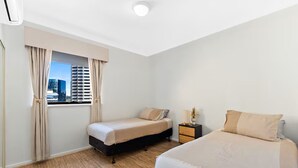 A hotel room with two beds, a window with curtains, a nightstand with a lamp, and a view of a cityscape. - Calm Central - A Sepal Stay (Perth)