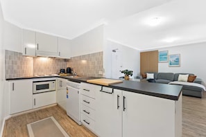 A modern kitchen with white cabinets, a microwave, and a dishwasher. There is a wooden countertop and a small island with a cutting board. - Calm Central - A Sepal Stay (Perth)