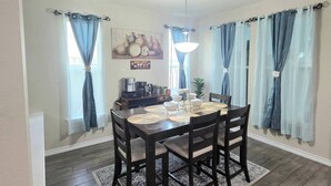 Un comedor con una mesa de madera, sillas, un tapete y cortinas.