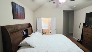 Un dormitorio con cama, ventilador de techo, un cuadro y una puerta que da a otra habitación.