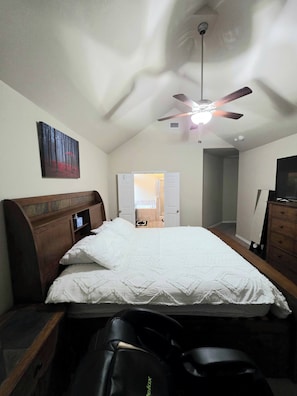 Ein Schlafzimmer mit einem Bett, einem Deckenventilator, einem Gemälde und einer Tür zu einem anderen Raum.