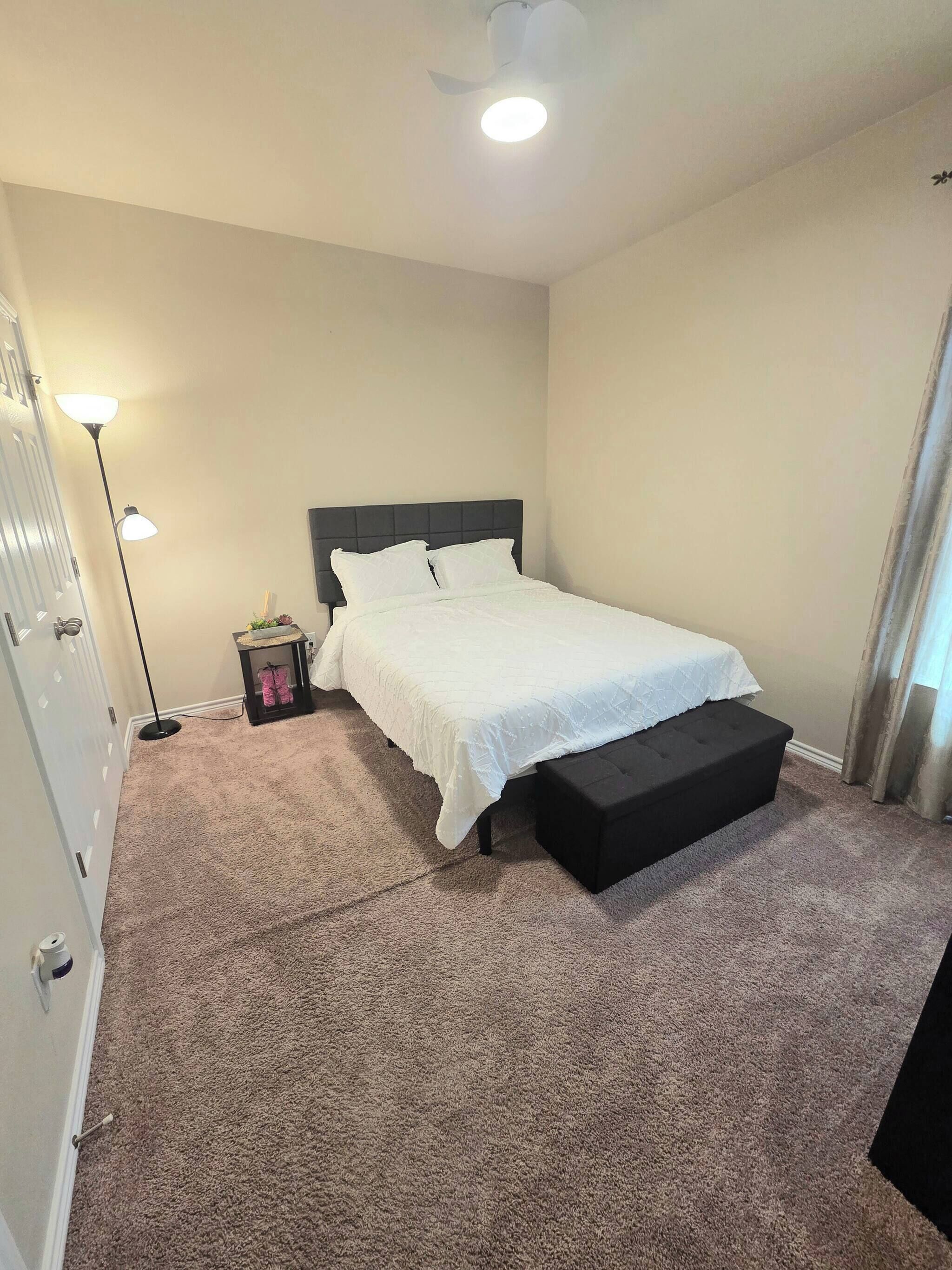 Un dormitorio con cama, lámpara de noche y ventilador de techo.