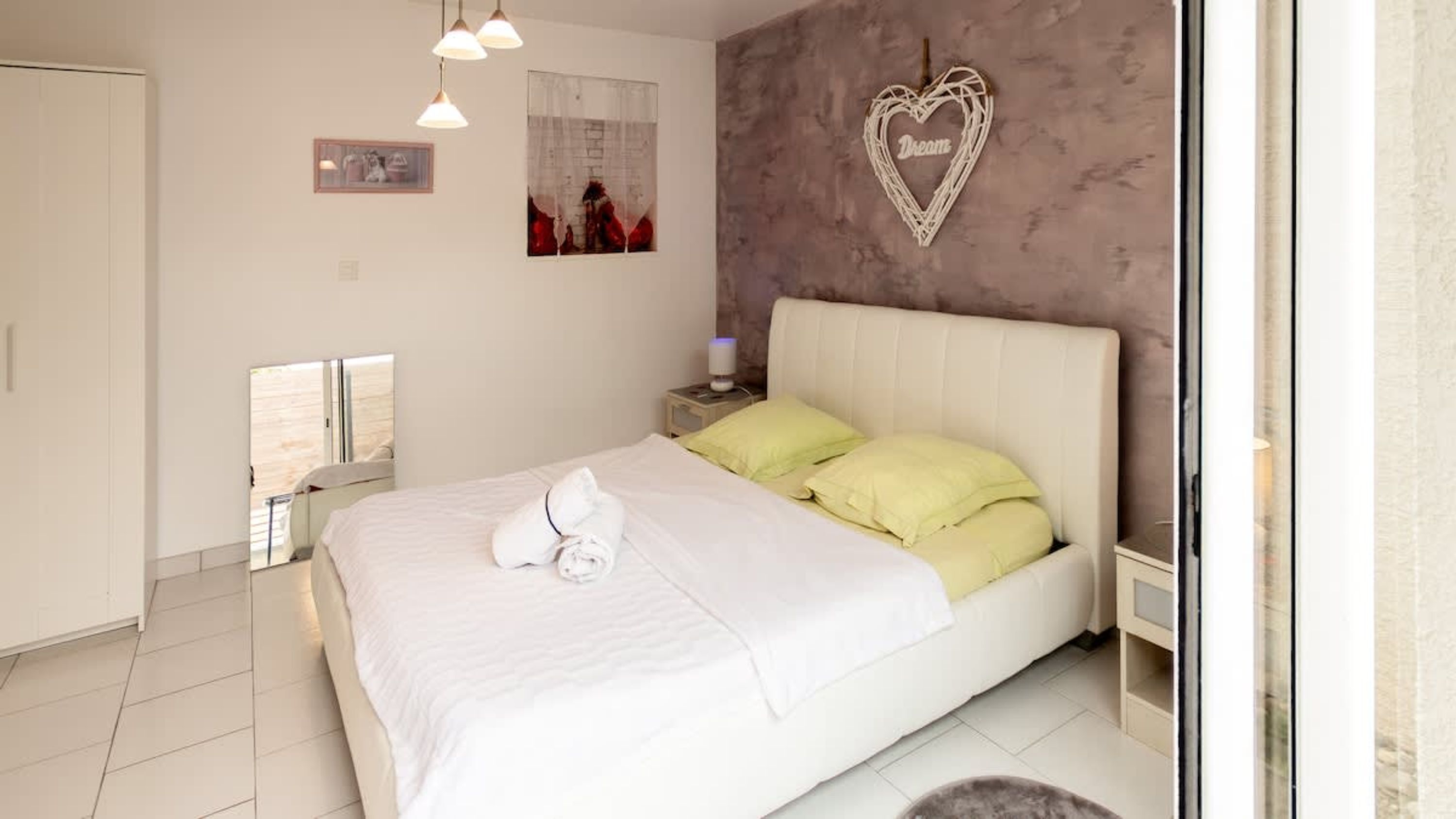 Une chambre à coucher avec un lit, des oreillers, un objet décoratif en forme de cœur, une table de chevet et un miroir.