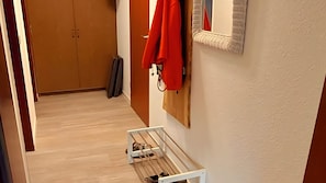 Ein Flur mit Holzboden, einem Kleiderständer mit roten Jacken, einem weißen Schrank und einer Tür mit Holzrahmen.
