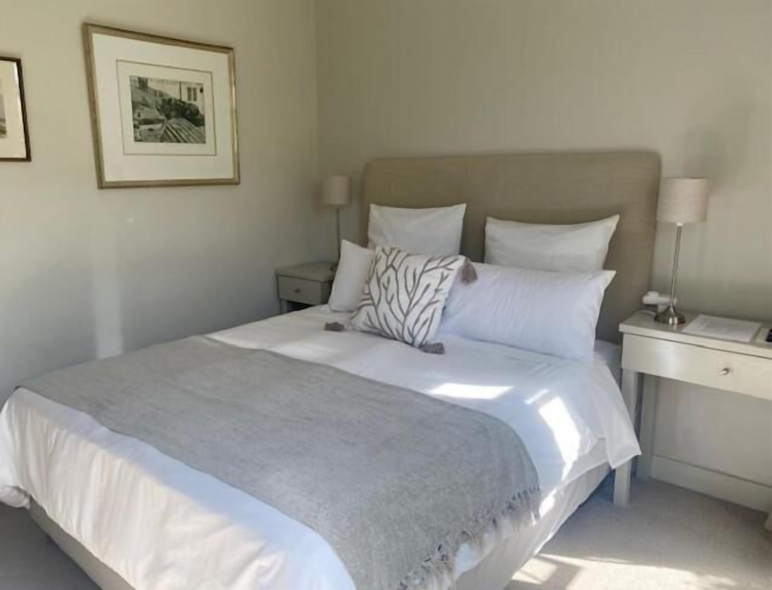 A neatly made bed with a grey blanket, a headboard, and two bedside tables with lamps.