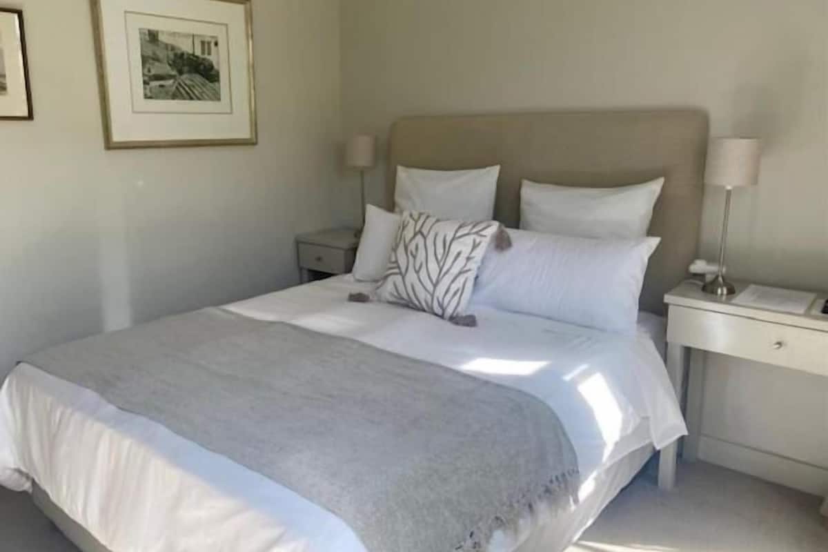 A neatly made bed with a grey blanket, a headboard, and two bedside tables with lamps.