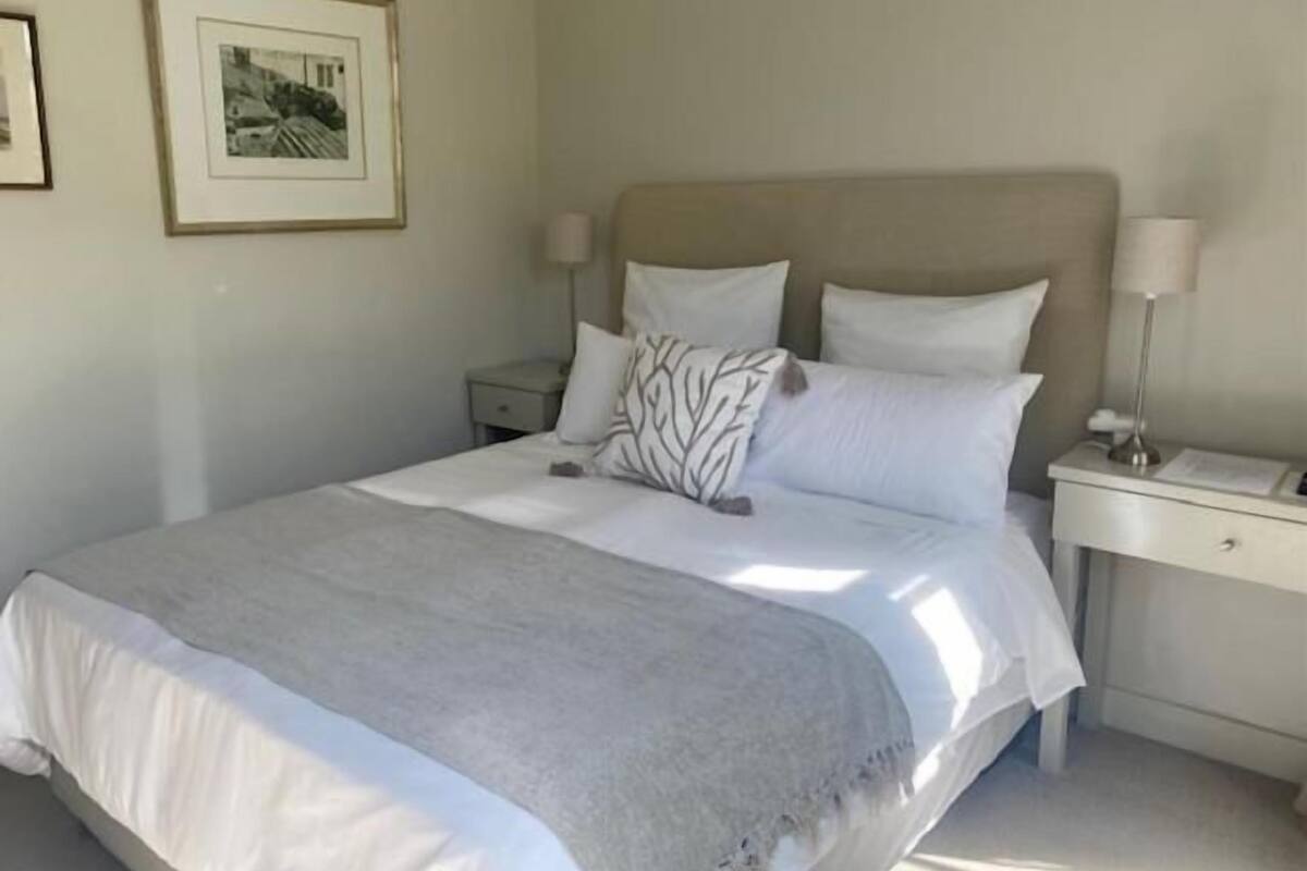A neatly made bed with a grey blanket, a headboard, and two bedside tables with lamps.