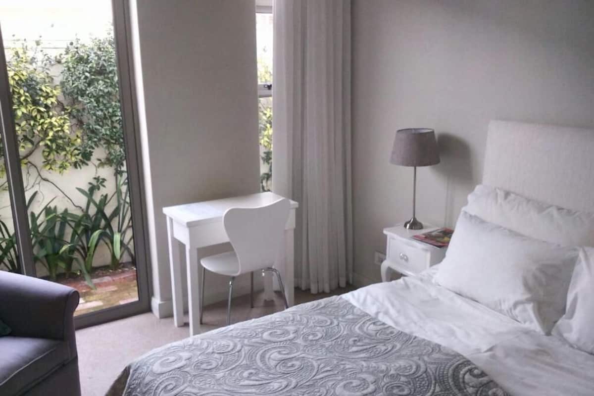 A bedroom with a bed, a desk, a chair, a nightstand, and a lamp.