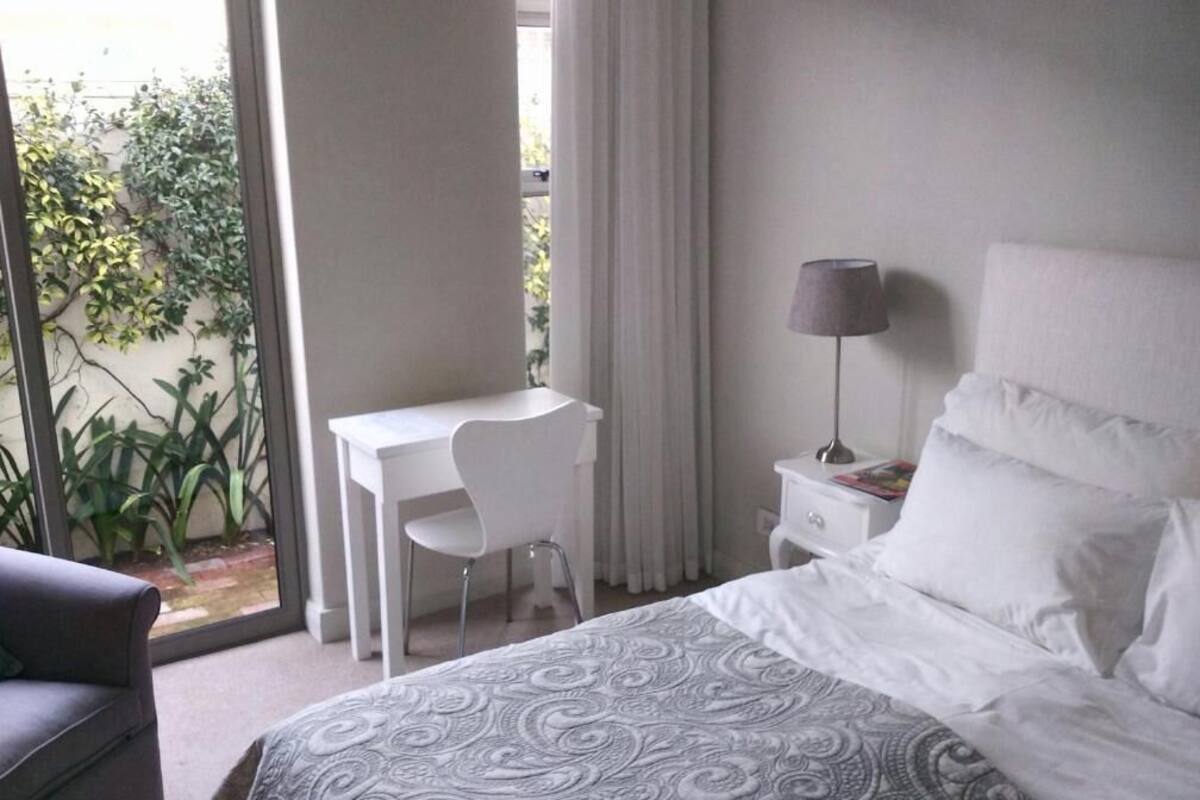 A bedroom with a bed, a desk, a chair, a nightstand, and a lamp.