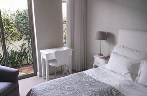 A bedroom with a bed, a desk, a chair, a nightstand, and a lamp. - 23 Grace (Cape Town)