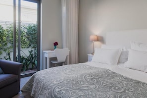 Una habitación de hotel con cama, escritorio, silla, lámpara y vista a zonas verdes por una ventana.