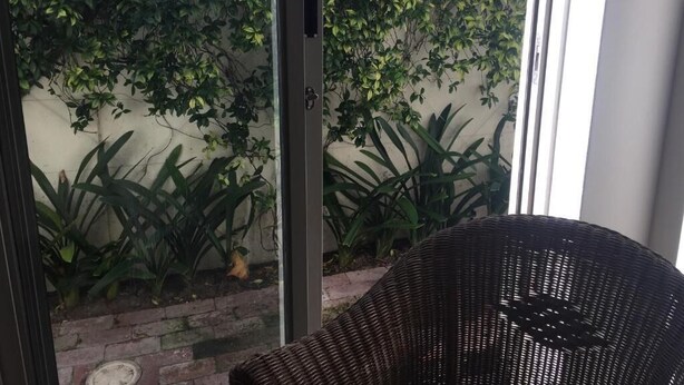 A wicker chair in a room with a glass door leading to a garden with various plants. - 23 Grace (Cape Town)