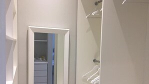 Pasillo que conduce a un baño con ducha, espejo y un perchero con juego de perchas blancas.