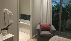 A modern bathroom with a bathtub, a chair with a red pillow, and a potted orchid. - 23 Grace (Cape Town)