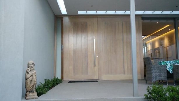 A modern entrance with a wooden door, a stone statue, and a seating area with wicker furniture. - 23 Grace (Cape Town)