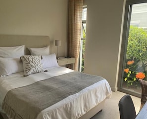 A bedroom with a bed, bedside table, lamp, and a view of greenery through a window. - 23 Grace (Cape Town)