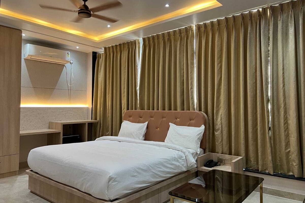 Ein modernes Hotelzimmer mit einem großen Bett, einem Nachttisch, einem Deckenventilator und Blick durch Vorhänge nach draußen.
