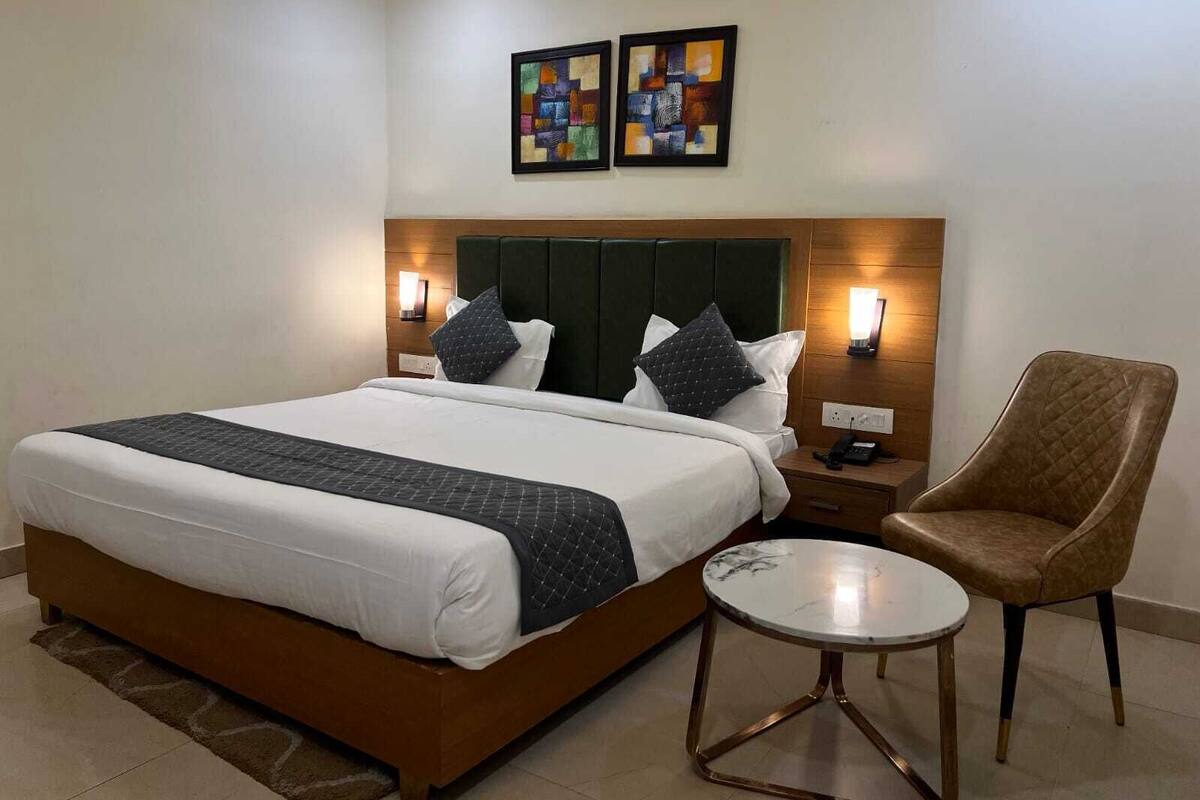 Ein Hotelzimmer mit einem großen Bett, zwei Wandbildern, einem Nachttisch mit Lampe, einem Sessel und einem kleinen runden Tisch.
