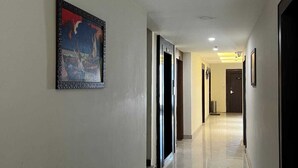 Un pasillo largo y bien iluminado con piso pulido, puertas a la derecha y un cuadro en la pared izquierda.