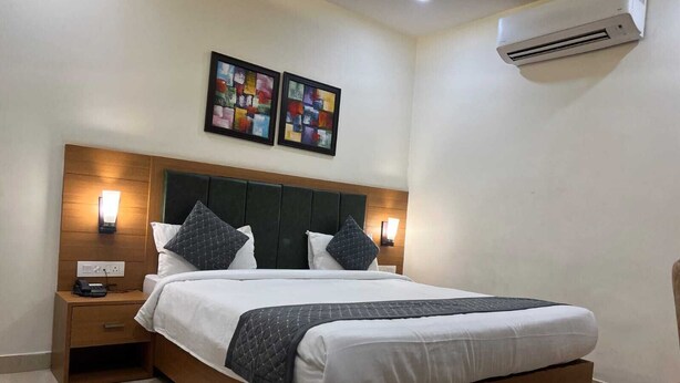 Una habitación de hotel con una cama de madera, dos unidades de aire acondicionado fijadas a la pared y dos cuadros enmarcados sobre la cama.