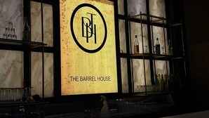 Un bar con un letrero que dice 'THE BARREL HOUSE' y estanterías llenas de botellas.
