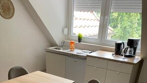 Una cocina compacta con una mesa y sillas, una ventana con persianas y una cafetera en la encimera.