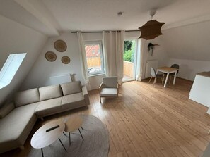 A modern living room with a sofa, a small table, a chair, and a dining area.