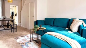 Un saló modern amb un sofà blau verd, una taula rodona petita amb una planta i una catifa colorida.