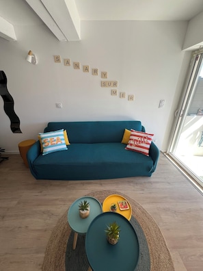 Un canapé de couleur turquoise avec des coussins, une lampe fixée au mur et un jeu de mots affiché sur le mur.