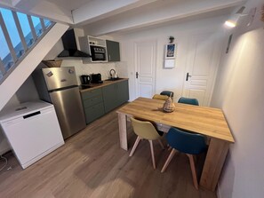 Eine kompakte Küche mit Einbauofen, Kühlschrank und Mikrowelle. Ein Esstisch mit Stühlen lädt zum Verweilen ein, und eine Treppe führt auf eine weitere Ebene.