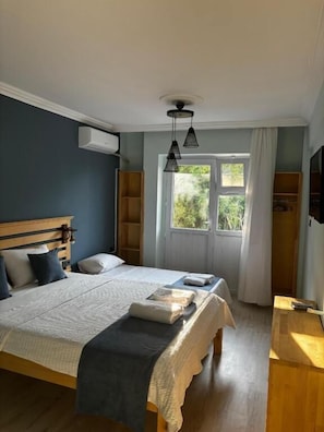 Ein Schlafzimmer mit einem Bett, Nachttischen, einem Fenster mit Vorhängen und einem Holzkopfende.