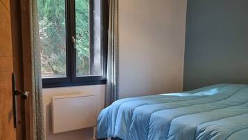 Et soveværelse med seng, et vindue med gardiner, en radiator, trægulv og en loftlampe.